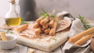 Traditional italian breadsticks grissini with rosemary, olive oil and sesame seeds on wooden countertop.