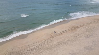Dalgıç kıyafeti giyen sörfçüler bulutlu bir öğleden sonra deniz kenarında sörf tahtası tutuyorlar..