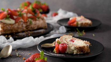 Strawberry cream roll cake slice on a black plate, garnished with fresh strawberries and cream, with a whole cake in the background on a dark surface clipart