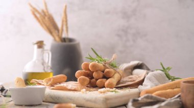 Kırsal ekmek çubukları sicimle bağlanmış ve ahşap bir tahtada biberiye ile süslenmiş, arka planda zeytin yağı ve buğday sapları ile sıcacık bir mutfak sahnesi yaratıyor.