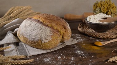 Köy ekmeği ahşap bir masada oturur. Etrafı buğday sapları, un ve merdaneyle çevrilidir.