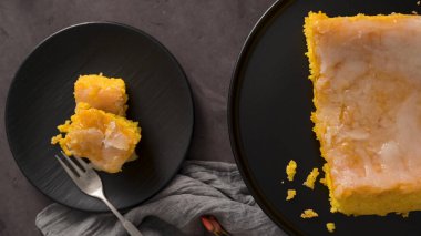 Bir dilim sarı pasta, siyah tabakta beyaz bir jöle, başka bir tabakta koca bir pastanın yanında..