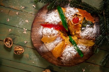 Geleneksel bir bayram tatlı ekmeği toz şekerle kaplanmış ve şekerli meyveler ve yeşil narenciye kabuğu ile süslenmiş, çam dallarıyla sade ahşap bir tahtanın üzerinde servis edilir.
