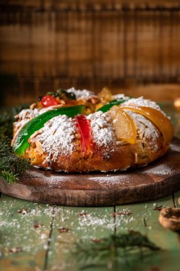 Geleneksel bir bayram tatlı ekmeği toz şekerle kaplanmış ve şekerli meyveler ve yeşil narenciye kabuğu ile süslenmiş, çam dallarıyla sade ahşap bir tahtanın üzerinde servis edilir.