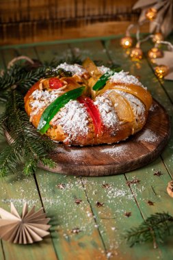 Geleneksel bir bayram tatlı ekmeği toz şekerle kaplanmış ve şekerli meyveler ve yeşil narenciye kabuğu ile süslenmiş, çam dallarıyla sade ahşap bir tahtanın üzerinde servis edilir.