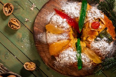 Geleneksel bir bayram tatlı ekmeği toz şekerle kaplanmış ve şekerli meyveler ve yeşil narenciye kabuğu ile süslenmiş, çam dallarıyla sade ahşap bir tahtanın üzerinde servis edilir.