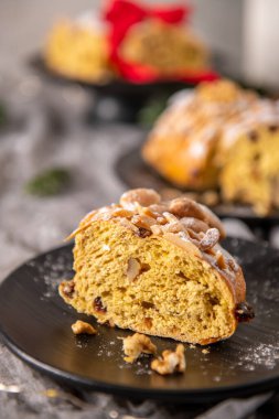 Geleneksel bir Portekiz Noel pastası olan Bolo Rainha 'nın cömert bir dilimi siyah bir tabakta sunuluyor. Badem ve pudra şekeri ile kaplandığında, zengin, meyveli bir iç mekan sergiliyor..