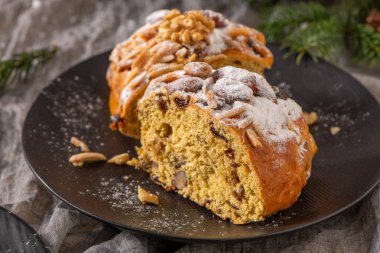 A generous slice of Bolo Rainha, a traditional Portuguese Christmas cake, is displayed on a dark plate. Its rich interior, studded with nuts and fruit, is dusted with powdered sugar. clipart