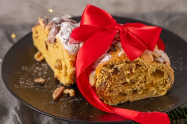 Bolo Rainha 'nın canlı kırmızı bir kurdeleyle süslenmiş şenlikli dilimi. Bu geleneksel Portekiz Noel pastası fındık ve meyvelerle dolu, bayram kutlamalarına hazır..
