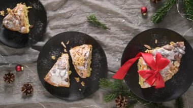 Bayramlık Bolo Rainha, kırmızı kurdeleyle bağlanmış siyah tabakları Noel dekorunun ortasında dilimliyor.