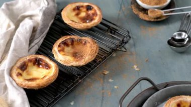 Beyaz tarçınlı siyah bir askıda üç Portekizli muhallebi tartı ve gri arka planda kaşıklar.