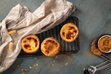 Soğutma rafında taze pişmiş üç Portekiz kremalı tartı keten bez ve tarçın serpilmeye hazır.