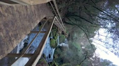 Dolambaçlı ahşap bir geçit Cascata do Outeiro yakınlarındaki çağlayan bir şelaleye doğru gidiyor. Yol, Oliveira de Azemis 'teki nehir manzarası ve çevresindeki ormanı gösteriyor..