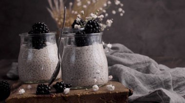 Böğürtlenli Chia pudingi, karanlık bir masada cam kavanozlarda üç porsiyon..