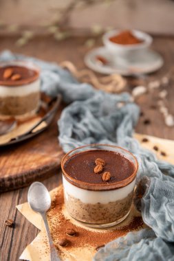 Bir bardakta tiramisu chia pudingi, kakao tozu ve kahve çekirdekleri ile kaplı, kırsal bir arka plan, yumuşak kumaş, ve kaliteli bir kaşık