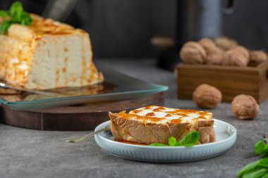Bir dilim molotof, arkaplanda kalan pudingin geri kalanıyla birlikte bir tabakta, tatlı şurupla süslenmiş ve taze nane ile süslenmiş geleneksel karamelize edilmiş yumurta beyazı puding var.