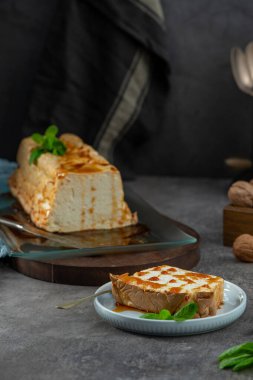 Bir dilim molotof, karamel şurubuyla süslenmiş ve naneyle süslenmiş geleneksel karamelize edilmiş yumurta beyazı puding, arka planda bütün pudingin bulunduğu bir tabakta bulunuyor.