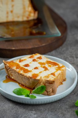 Cazip bir molotof dilimi, geleneksel karamelize edilmiş yumurta akı pudingi, cömertçe tatlı şurubu serpiştirilmiş ve taze nane yapraklarıyla süslenmiş, açık mavi bir tabakta duruyor.