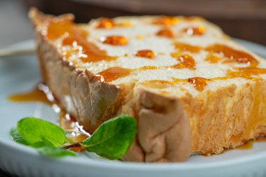 Yakın plan çekimde, karamelize edilmiş yumurta beyazlarından yapılmış, bol bol kehribar şurubu serpiştirilmiş ve yumuşak mavi bir tabakta parlak yeşil nane yapraklarıyla süslenmiş geleneksel bir puding olan tek bir molotof bulunur.