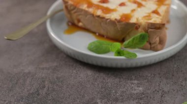 Altın karamel sosuyla süslenmiş ve taze nane yapraklarıyla süslenmiş geleneksel molotof pudinginin lezzetli bir dilimi küçük yuvarlak bir tabakta servis ediliyor..