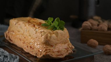 Lezzetli bir puding, karamelize edilmiş üstü parlak, canlı yeşil nane ile süslenmiş, parlak cam bir tabakta sunulmuş..