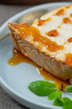 Baştan çıkarıcı bir yakın çekim sergileniyor geleneksel karamelli yumurta akı pudingi, bol bol karamel şurubu serpiştirilmiş ve açık mavi bir tabakta parlak yeşil nane yapraklarıyla süslenmiş.