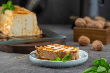Tatlı şurupla süslenmiş ve taze nane ile süslenmiş geleneksel bir karamelize edilmiş yumurta beyaz pudingi, açık mavi bir tabakta tüm pudingin yanında.
