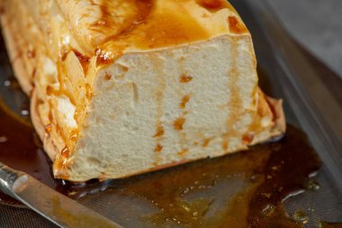 Yakın plan çekimde, koyu bir yüzey üzerine bol kehribar şurubu serpiştirilmiş klasik bir Portekiz karamelli yumurta beyaz pudingi önemli miktarda molotof sergilenir.