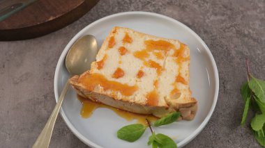 Altın karamel serpilmiş ve taze nane filizi ile süslenmiş, yukardan yakalanmış yuvarlak beyaz bir kaşıkla sunulmuş, geleneksel molotof pudinginden tek bir dilim..