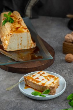 Bir dilim molotof, şekerli ve naneyle süslenmiş geleneksel karamelize edilmiş yumurta akı pudingi, arka planda kalan pudingin geri kalanıyla birlikte bir tabakta oturur.