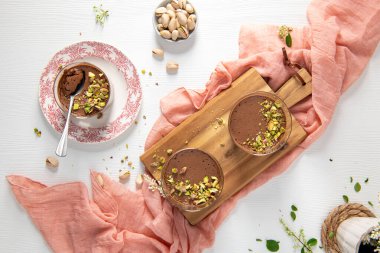 Üç çikolatalı puding, fıstıklı, bir kase fındıklı ve beyaz ahşap bir masada pembe çarşaflı.