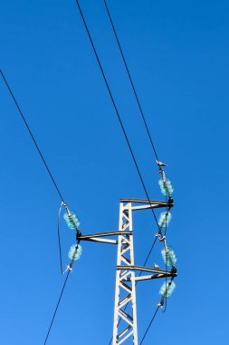 Açık mavi gökyüzü, Portekiz 'in Ovar şehrinde sayısız elektrik hattı ve mavi cam yalıtkanlarıyla beyaz metal elektrik direğini vurguluyor. Bir koluna tünemiş bir kuş..