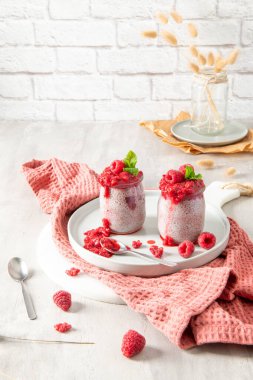 İki ayrı cam kavanoz ev yapımı ahududu chia tohumu pudingi beyaz bir tabakta sunuluyor. Sağlıklı tatlı, zengin bir ahududu kompostosu ve bir tutam nane ile süslenmiş taze ahududu ile kaplıdır. Kompozisyon daha büyük bir s 'nin parçası.