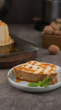 Ekstra karamel serpilmiş ve taze nane ile süslenmiş, küçük beyaz bir tabakta servis edilen lezzetli bir dilim karamelli molotof..