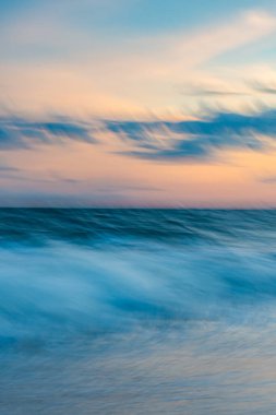 Gün batımında sahilde uzun süre soyut deniz manzarası, akan okyanus suyu hareketleri ve renkli gökyüzü.