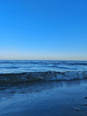 Dalgalar yavaşça kıyıya vuruyor engin ufuk ve mavi gökyüzü