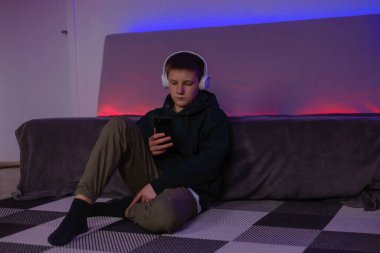 Teenage boy using phone in his room with neon light.