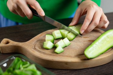 Kadın sebze salatası pişirmek için salatalık kesiyor. Ev mutfağı.