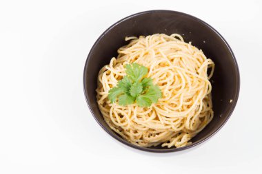 Sarı biberli spagetti. Beyaz arka planda siyah bir kasede kişniş ile süslenmiş.