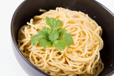 Sarı biberli spagetti. Beyaz arka planda siyah bir kasede kişniş ile süslenmiş.