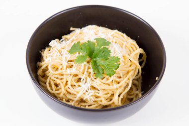 Beyaz arka planda siyah bir kasede kişniş ile süslenmiş rendelenmiş mozzarella peyniri ile kaplı sarı biberli spagetti.