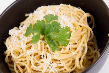 Beyaz arka planda siyah bir kasede kişniş ile süslenmiş rendelenmiş mozzarella peyniri ile kaplı sarı biberli spagetti.