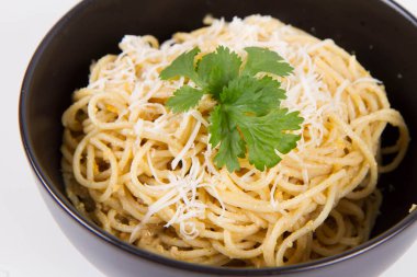 Beyaz arka planda siyah bir kasede kişniş ile süslenmiş rendelenmiş mozzarella peyniri ile kaplı sarı biberli spagetti.