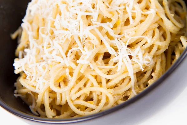白い背景に黒いボウルにすりおろしたモッツァレラチーズで覆われた黄色のコショウペストスパゲティ — ストック写真