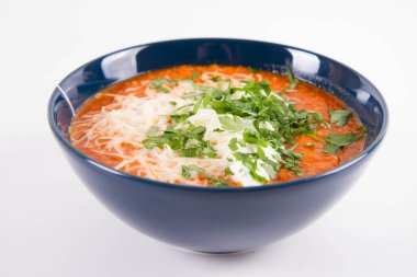 Kremayla servis edilen İtalyan domates çorbası, mozzarella peyniri ve beyaz arka planda bir kasede taze maydanoz.