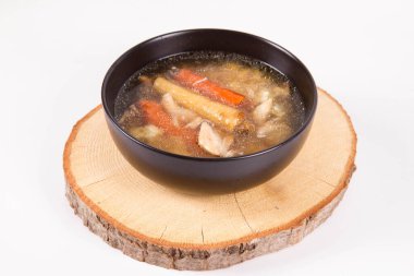 Chicken soup with noodle and carrot and parsley roots, chicekn meat visible, in a bowl on a wooden pad