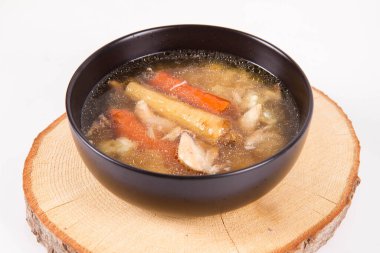 Chicken soup with noodle and carrot and parsley roots, chicekn meat visible, in a bowl on a wooden pad