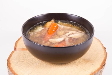 Chicken soup with noodle and carrot and parsley roots, chicekn meat visible, in a bowl on a wooden pad