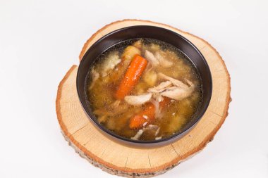 Chicken soup with noodle and carrot and parsley roots, chicekn meat visible, in a bowl on a wooden pad