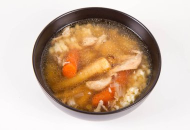 Chicken soup with noodle and carrot and parsley roots, chicken meat visible, in a bowl on a white background